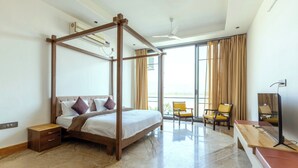 A modern hotel room with a four-poster bed, a sitting area with chairs, a desk, and a large window with curtains. - Heartland Ganga View Villa Jacuzzi &lift (Rishikesh)