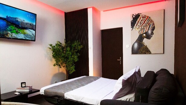 A modern hotel room with a bed, a flat-screen TV, a painting, and a potted plant.