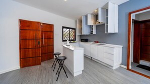 A modern kitchen with white cabinetry, a wooden door, and a small island with stools.