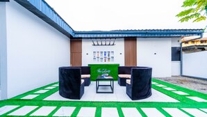 An outdoor seating area with a table and chairs, a green sign, and a wall with framed pictures.