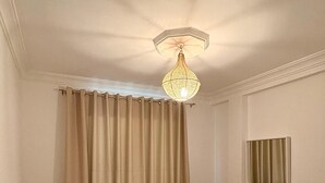 Une chambre à coucher avec un lit, une fenêtre avec des rideaux, un climatiseur fixé au mur et un luminaire au plafond.