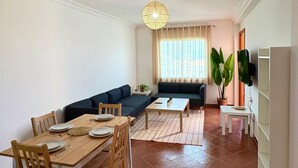 Un salon comprenant un coin repas, un canapé, un téléviseur et une grande fenêtre.
