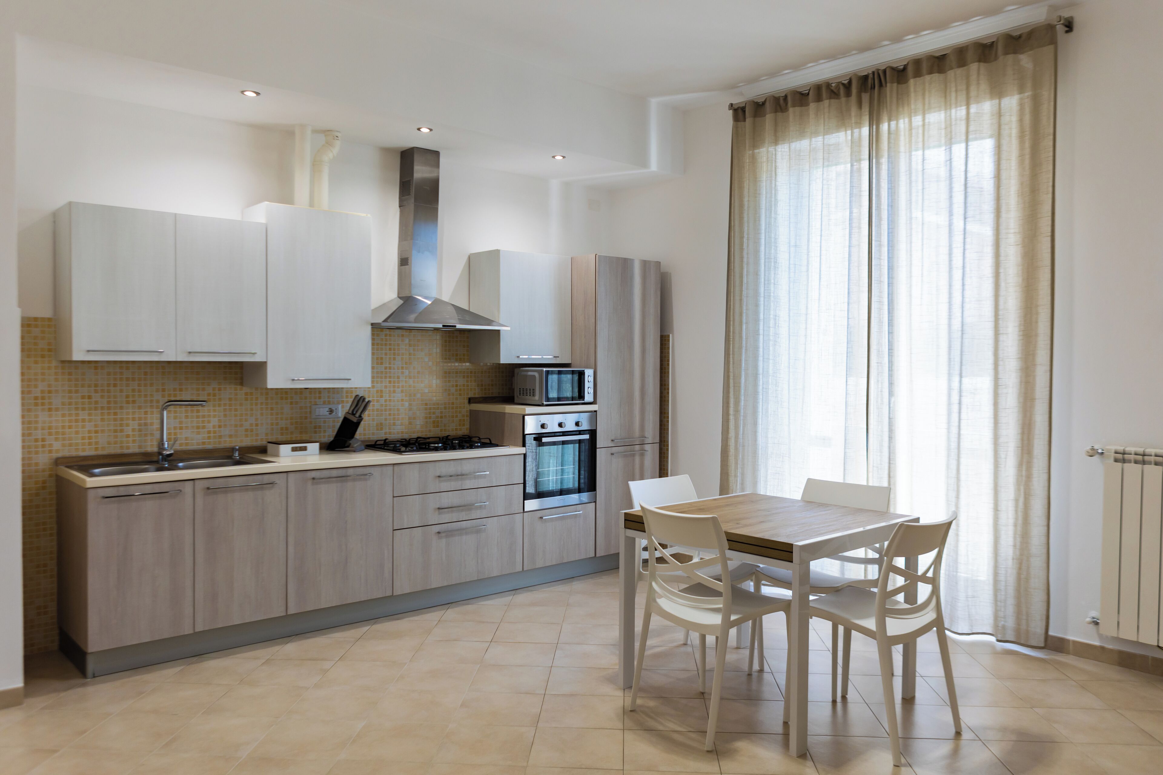 Une cuisine moderne avec des meubles en bois clair, une hotte en acier inoxydable et un coin repas comprenant une table et des chaises.
