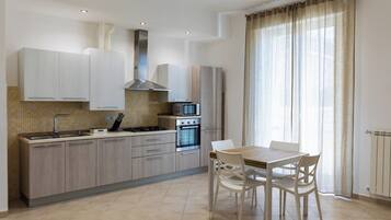Une cuisine moderne avec des meubles en bois clair, une hotte en acier inoxydable et un coin repas comprenant une table et des chaises.