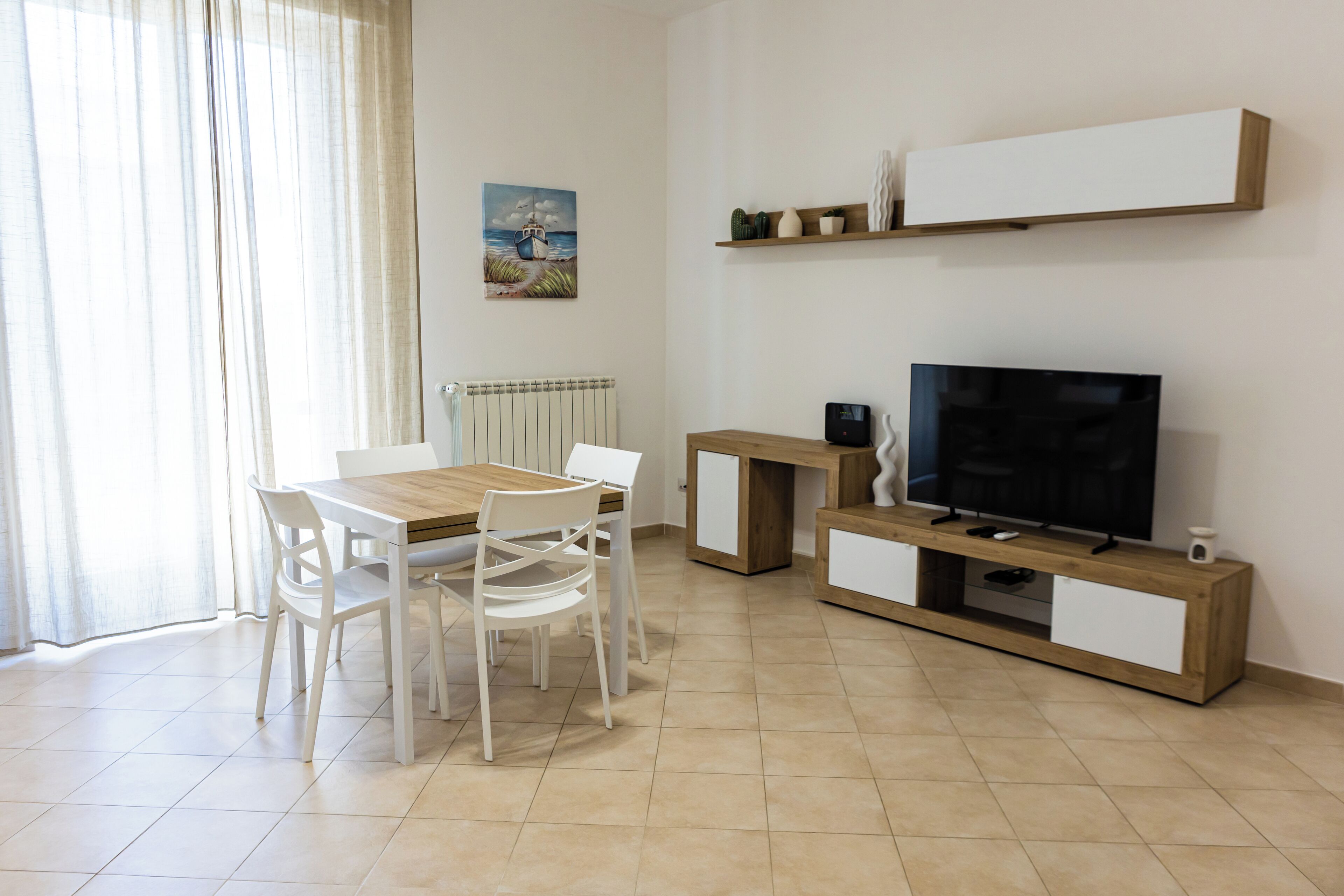 Un salon moderne avec une table à manger en bois, des chaises blanches, un téléviseur et un petit meuble.