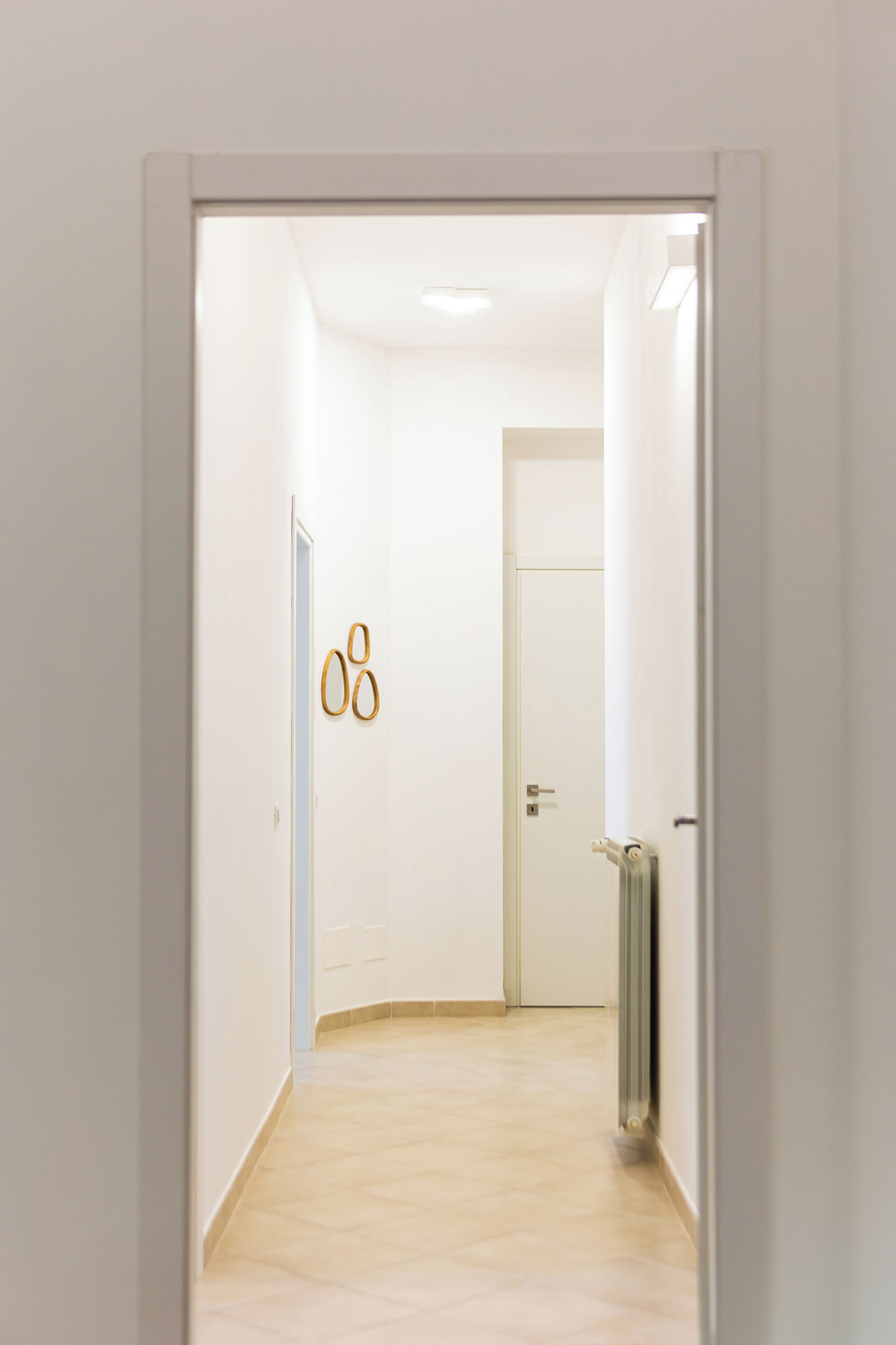 Un couloir avec une porte blanche, un radiateur et un interrupteur sur le mur.