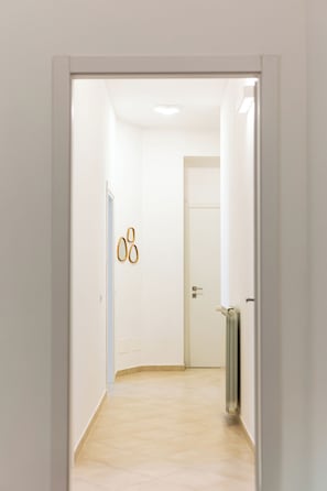 Un corridoio con una porta bianca, un termosifone e un interruttore sulla parete.