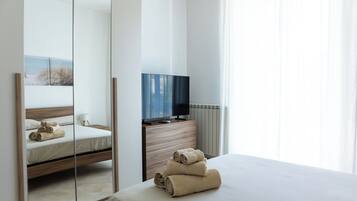 Une chambre d’hôtel moderne avec un grand lit, un téléviseur posé sur une commode en bois et un miroir qui reflète la pièce.