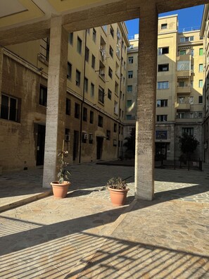 A courtyard with stone flooring, two potted plants, and a building with multiple balconies and windows.