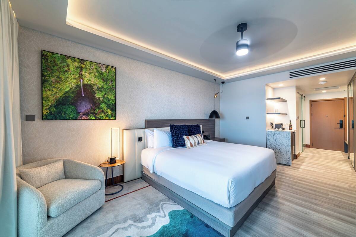 A modern hotel room with a large bed, a sofa, a desk, and a bathroom visible through an open door.