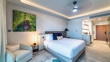 A modern hotel room with a large bed, a sofa, a desk, and a bathroom visible through an open door.
