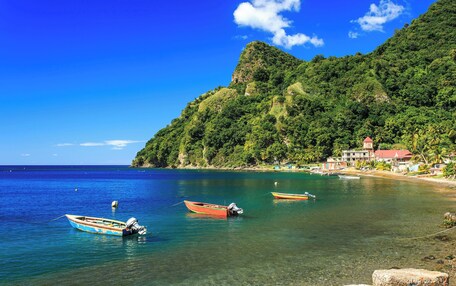A coastal scene with clear blue water, boats, and a mountainous backdrop.
