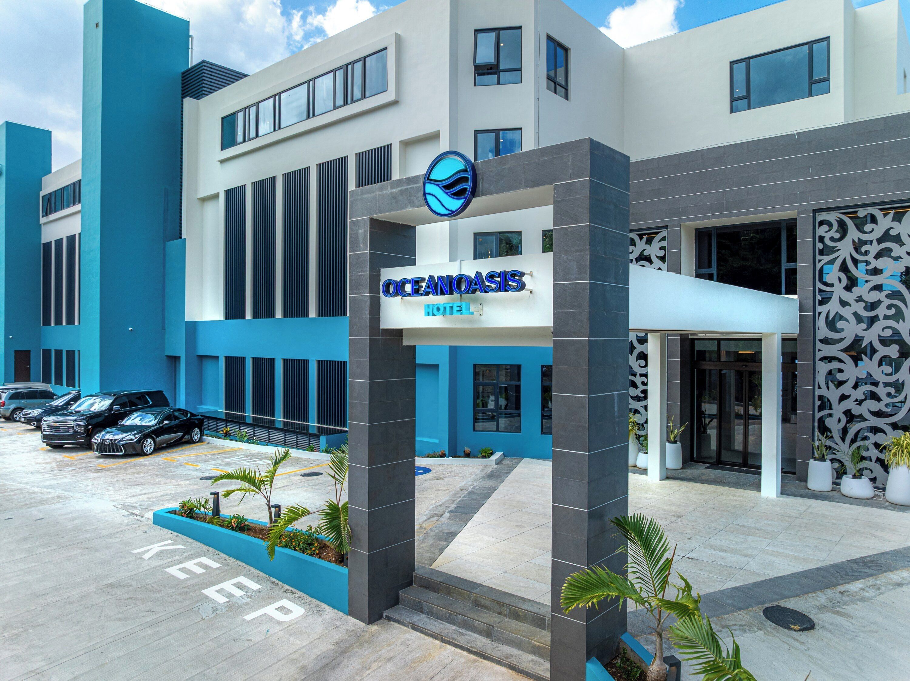 Exterior del Hotel Ocean Oasis con un diseño moderno, destacando una entrada imponente, un estacionamiento con varios coches y una fachada decorativa.