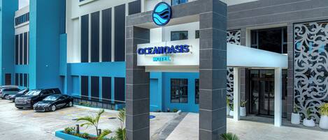 Exterior del Hotel Ocean Oasis con un diseño moderno, destacando una entrada imponente, un estacionamiento con varios coches y una fachada decorativa.