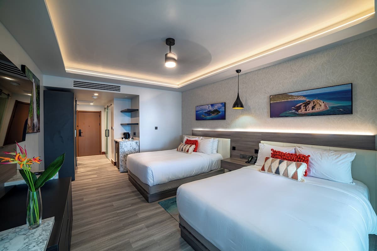 A modern hotel room with two beds, a desk, a vase with flowers, and a painting on the wall.