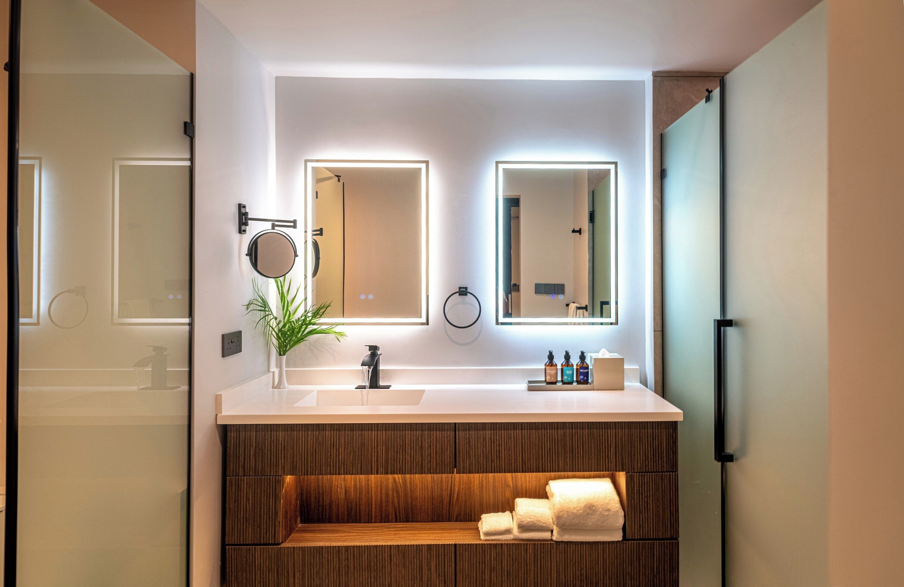 Un baño moderno con un tocador blanco, estantes de madera, un espejo y una planta.