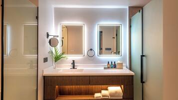 Un baño moderno con un tocador blanco, estantes de madera, un espejo y una planta.