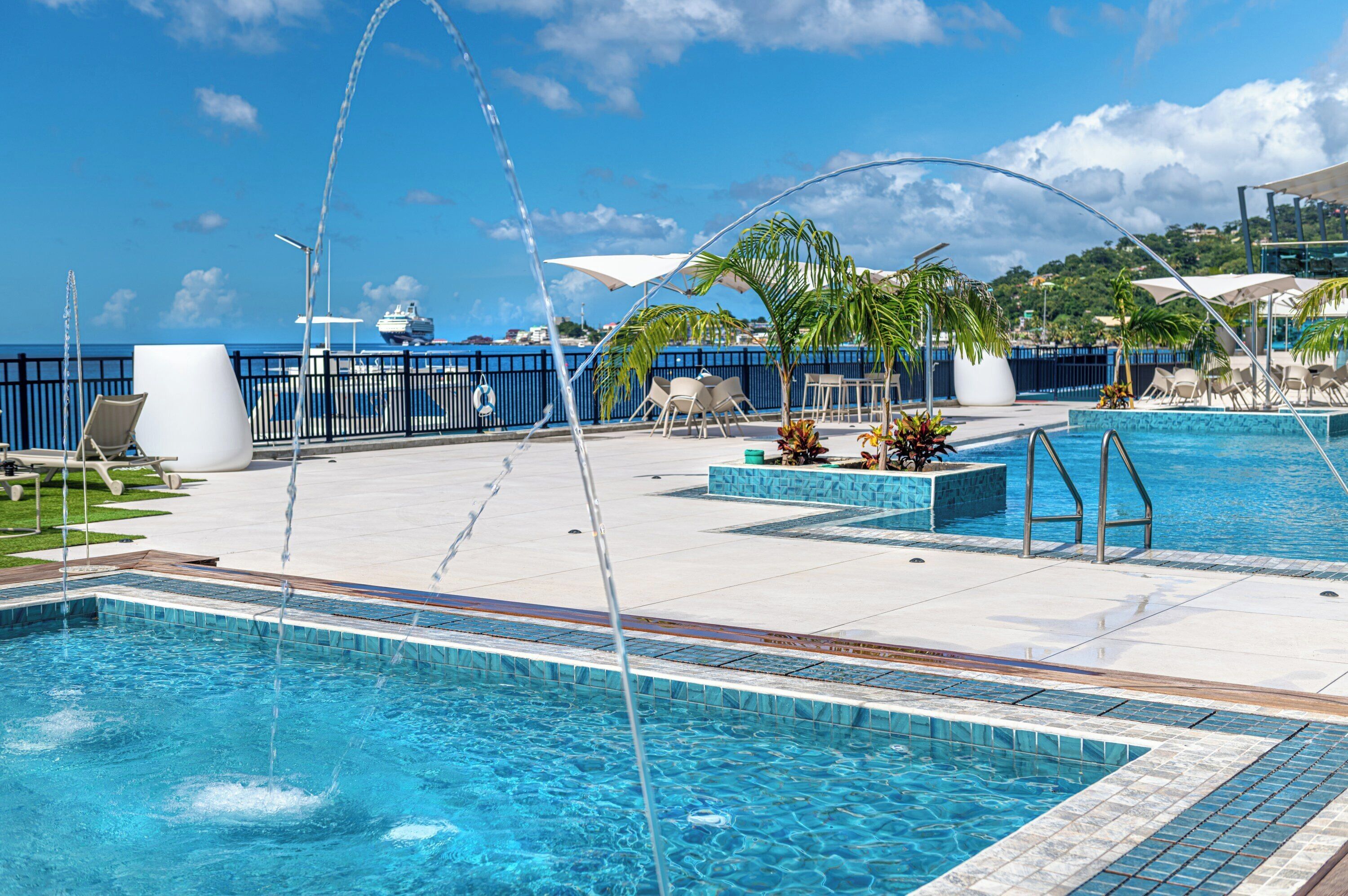 Área da piscina com vista desobstruída para o mar, espreguiçadeiras e uma fonte de água.