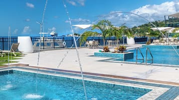 Área da piscina com vista desobstruída para o mar, espreguiçadeiras e uma fonte de água.