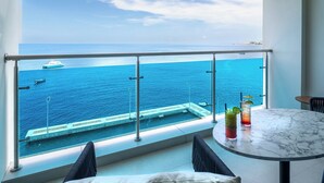 Un balcone con vista sul mare, una piscina e due bicchieri su un tavolo.