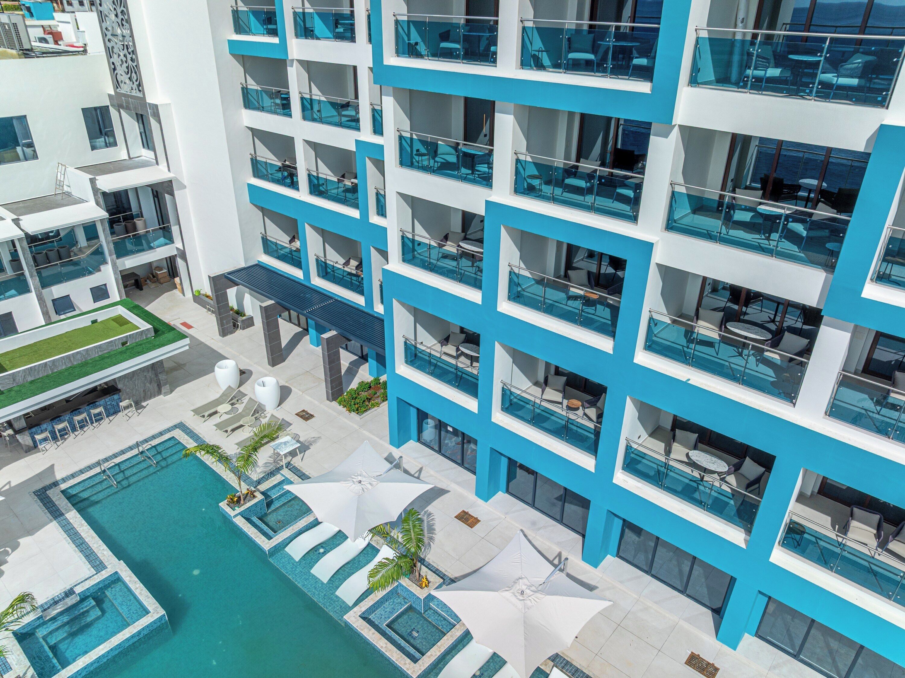 Un hotel moderno con varios balcones, piscina y zonas de estar al aire libre.