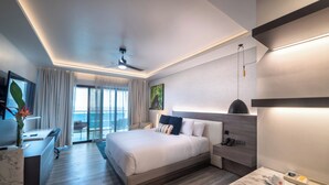 Camera d'albergo moderna con un ampio letto, una scrivania, una sedia e vista sull'oceano attraverso un'ampia porta scorrevole in vetro.