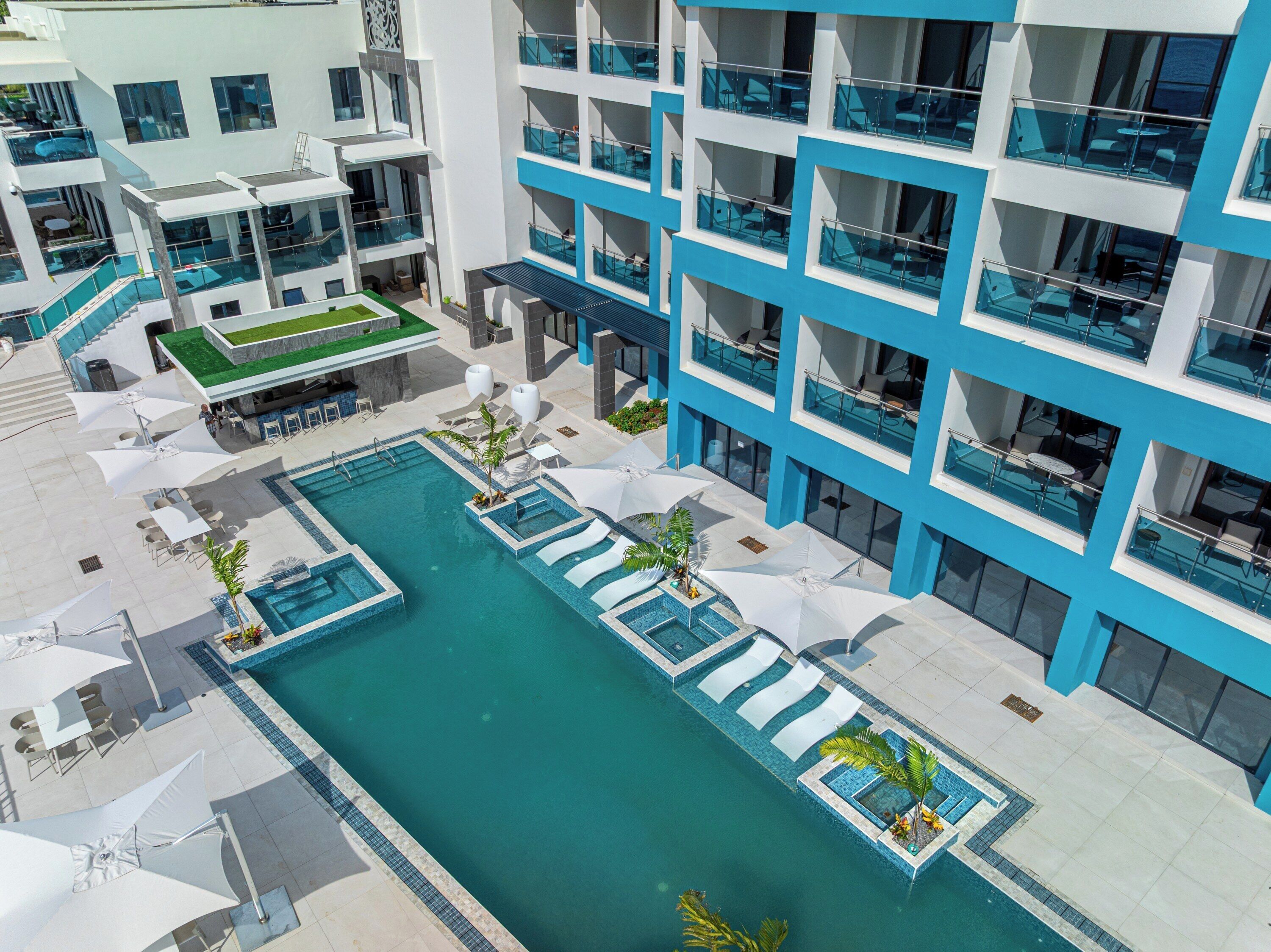 Un hotel moderno con piscina central, zona de estar exterior y bar en la azotea.