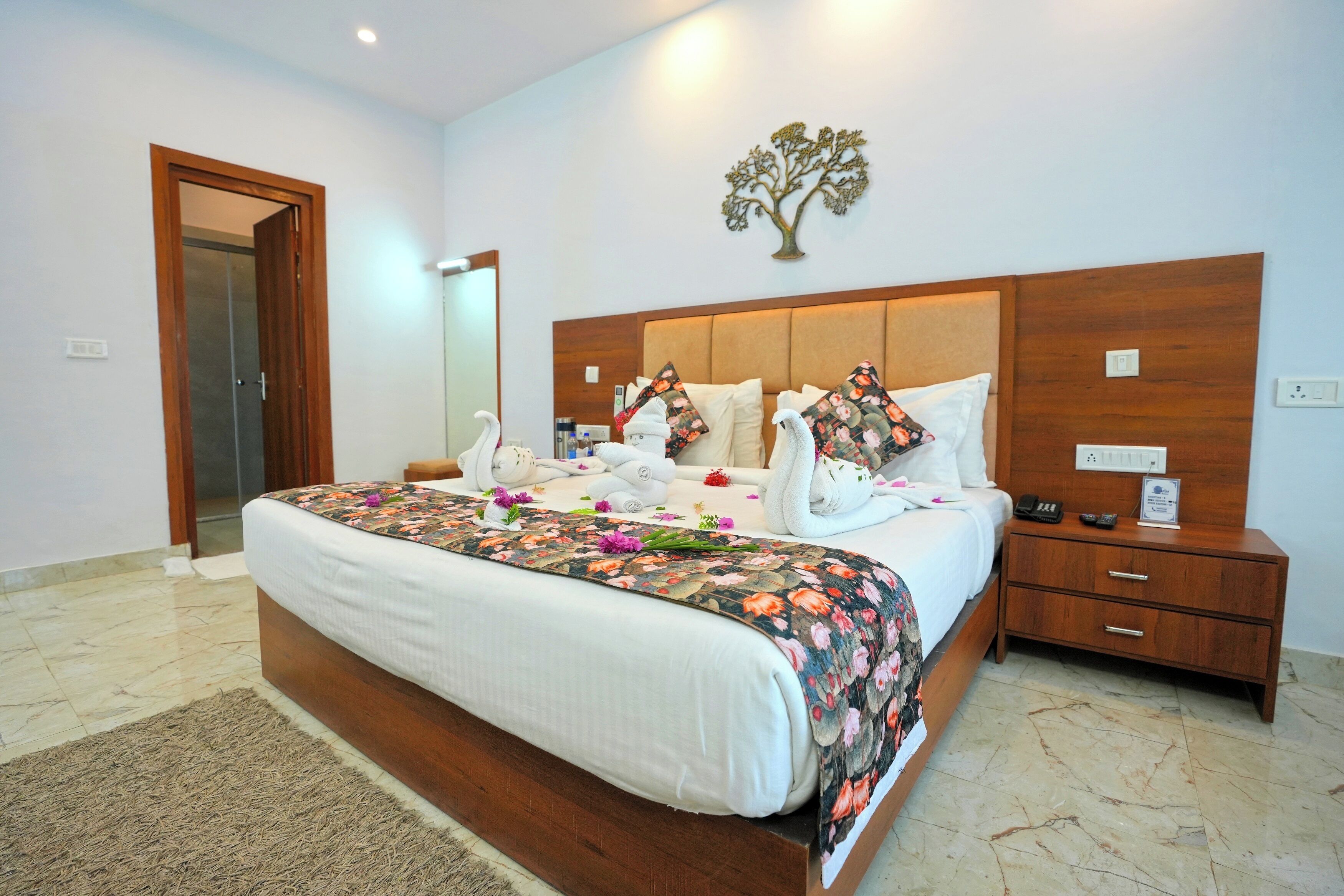 A neatly made bed with a floral bedspread, a wooden headboard, and a nightstand with a phone and a small item on it.