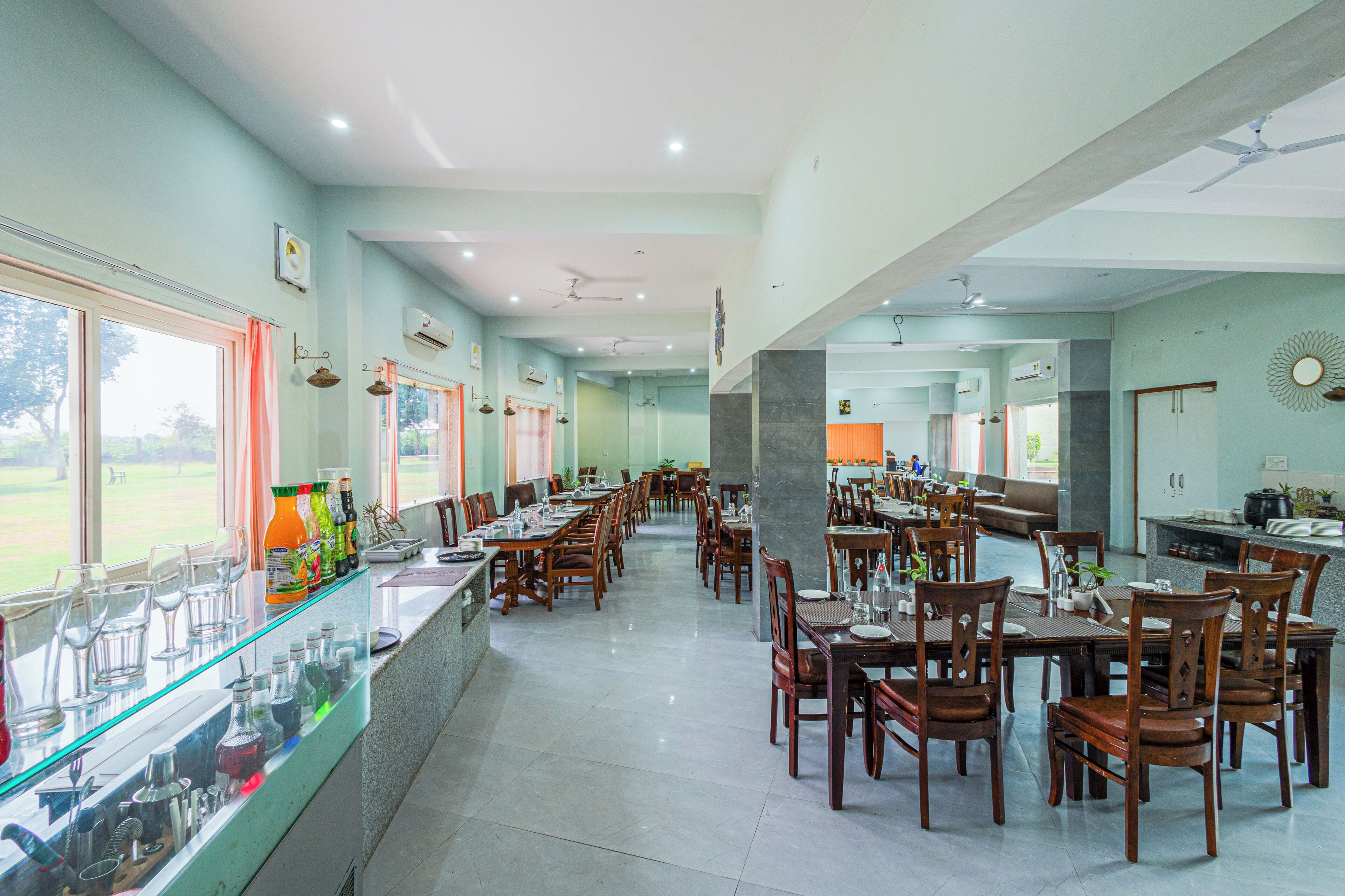 A spacious dining area with multiple tables and chairs, a bar with glassware, and large windows offering a view of the outdoors.