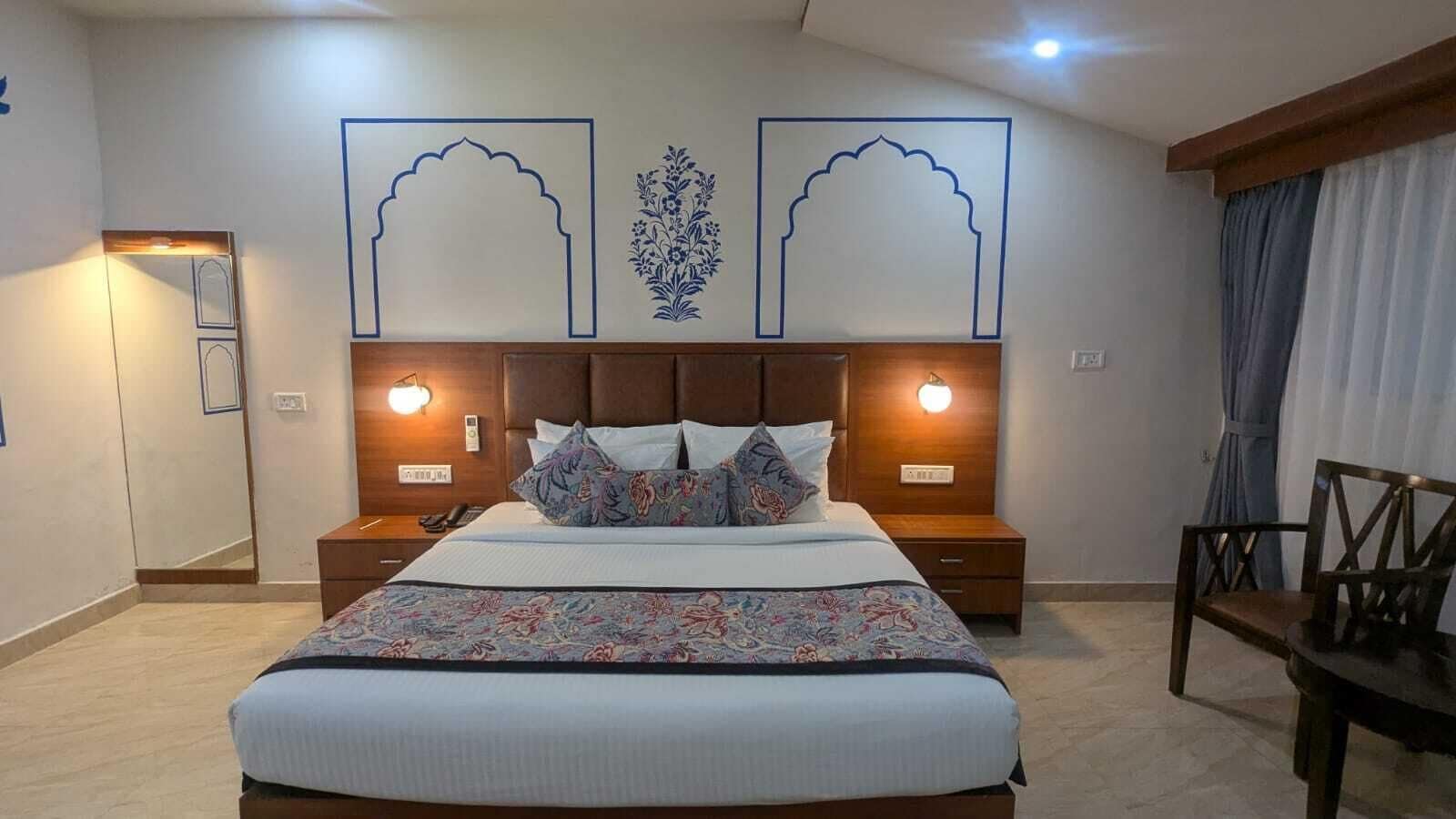 A hotel room with a large bed, two bedside tables with lamps, a chair, and decorative wall art.