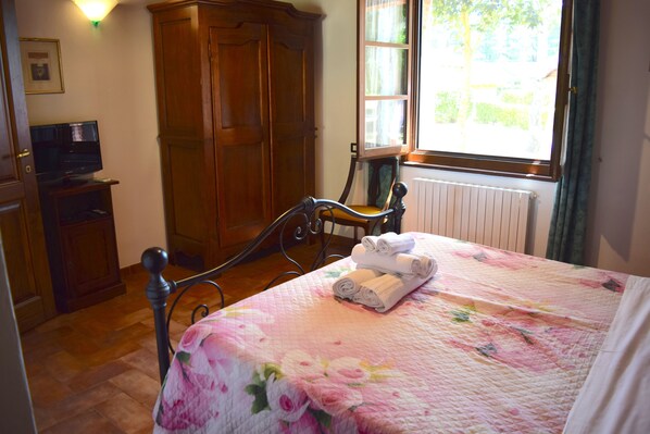Une chambre à coucher avec un lit, une armoire en bois, une télévision et une fenêtre avec des rideaux.