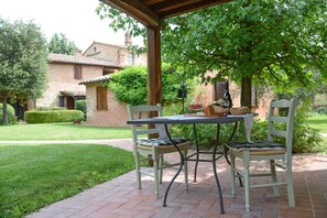 Une terrasse couverte avec une table et des chaises, une bouteille de vin et un panier de pain.