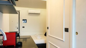 A compact hotel room with a kitchenette, a bed, an air conditioning unit, and a door with a lock. - [Torino] San Salvario Attic Room (Torino)