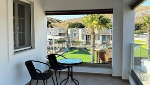 Un balcon avec une table et des chaises, une fenêtre et une vue sur une cour intérieure bordée de bâtiments en pierre et de palmiers.