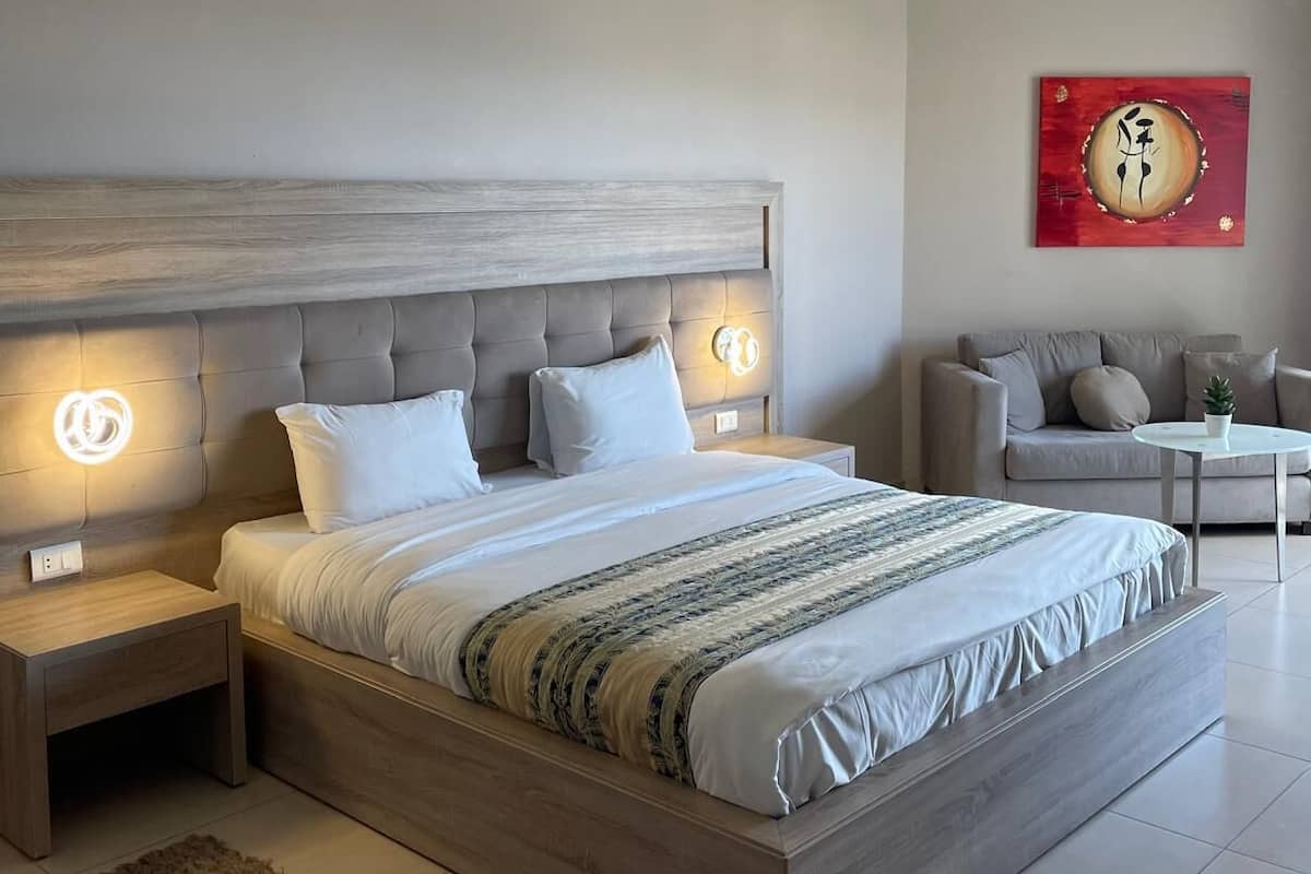 Un dormitorio moderno con una cama grande, dos mesitas de noche, un tapete mullido, un sofá y una obra de arte en la pared.