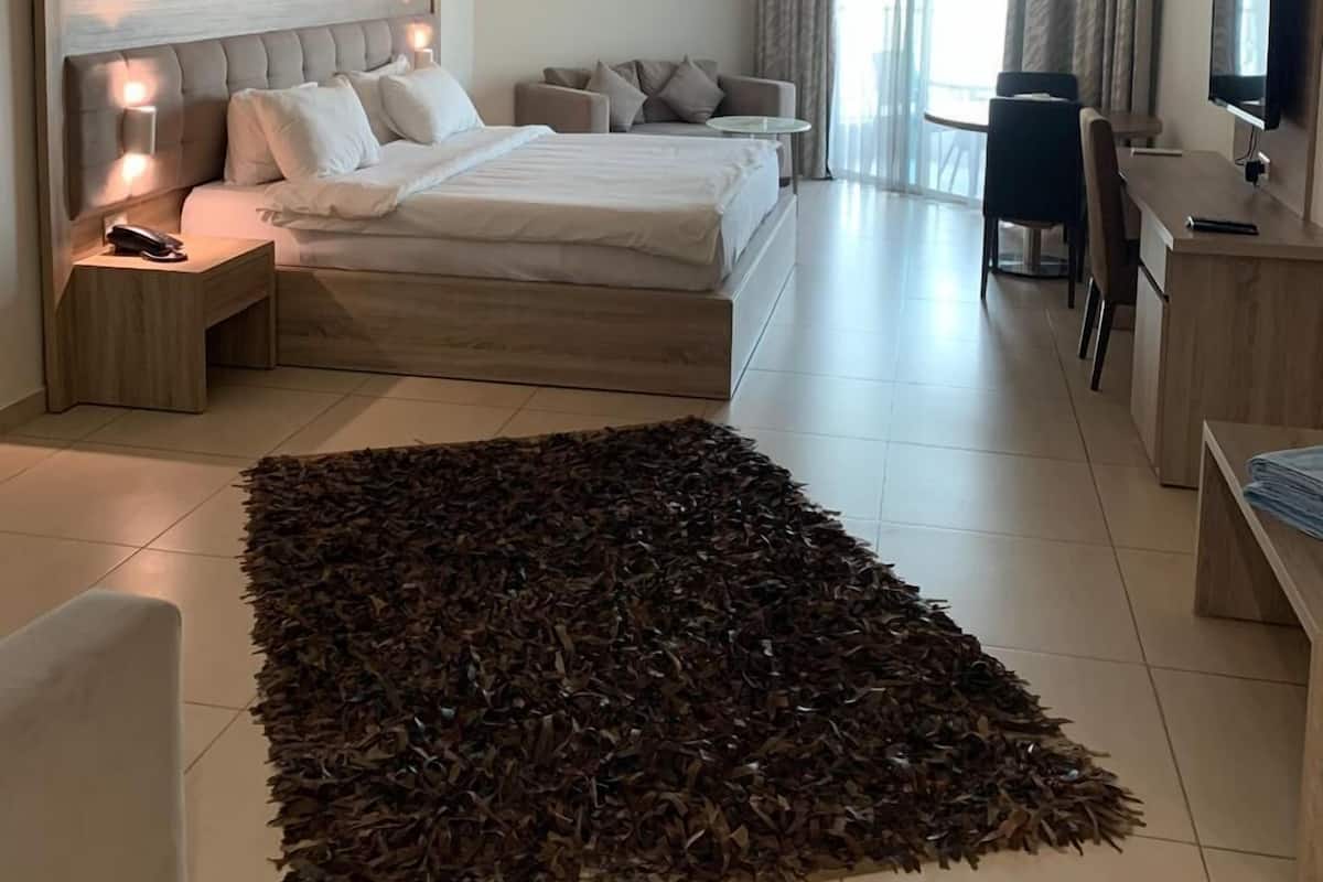 Habitación de hotel con cama, mesitas de noche, escritorio, silla, televisor y un amplio ventanal con cortinas.