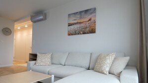 A modern living room with a light grey sofa, a wooden coffee table, and a painting of a sunset over a bridge. - RentPlanet - przy Dworcu Głównym (Poznań)