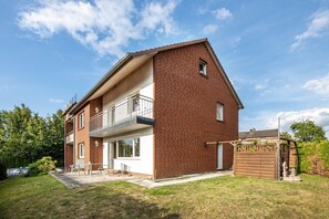 Une maison à deux étages, construite en briques, dotée d’un balcon, d’un garage et d’un petit jardin.