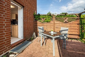 Une terrasse avec une table et des chaises, une clôture en bois et un mur en briques.