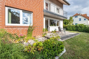 A two-story brick house with a balcony, a patio with a chair, and a well-maintained garden.