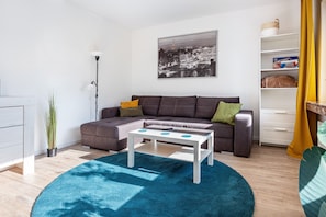 A living room with a sofa, a coffee table, a plant, a lamp, and a framed picture on the wall.