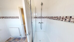 Un baño con ducha de vidrio, paredes con azulejos blancos y piso de baldosas.