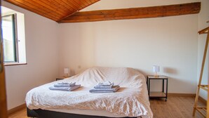 Ein Schlafzimmer mit Holzbalkendecke, einem Bett mit weißer Bettdecke, zwei Nachttischen mit Lampen und einem Holzboden.