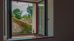 Ein Schlafzimmer mit großem Fenster, Holzboden und einem Bett mit einem gemusterten Bettbezug.