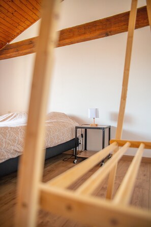 A bedroom with a wooden ceiling, a bed with a patterned bedspread, a small bedside table with a lamp, and a power outlet.