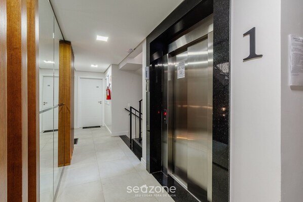 A modern hallway with a glass partition, an elevator, and a fire extinguisher.