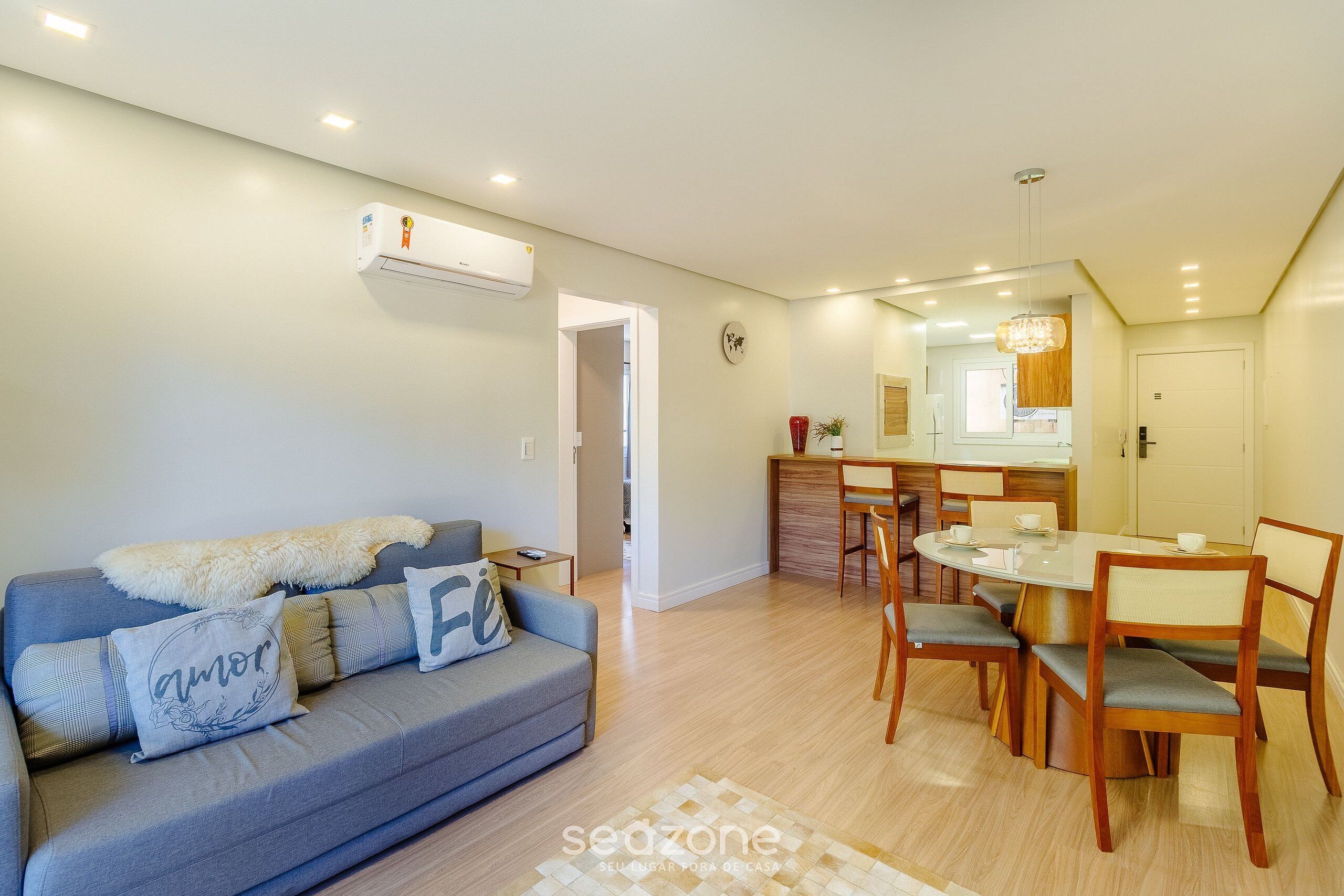 A modern living room with a grey sofa, wooden dining table, and chairs.