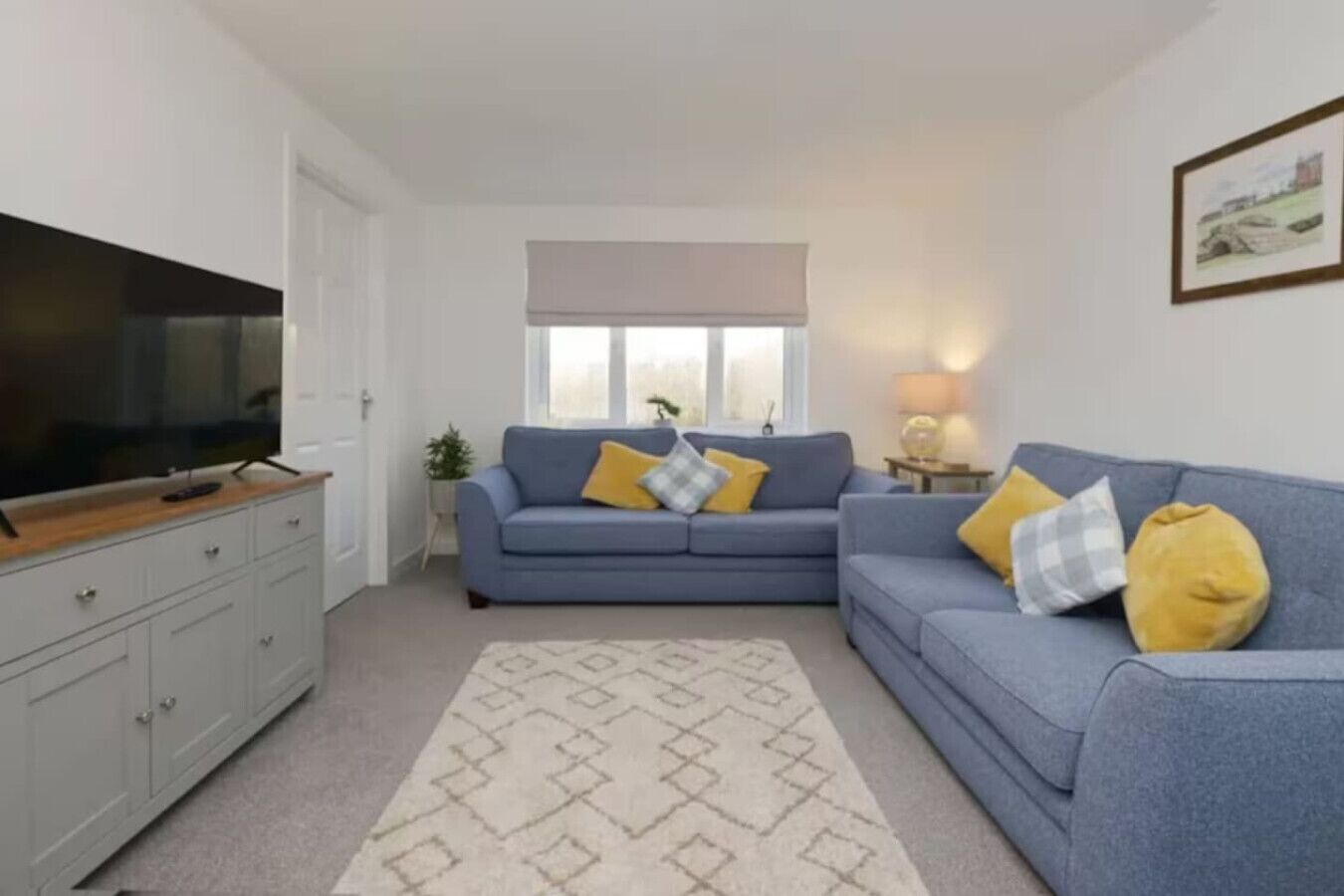 Ein Wohnzimmer mit grauem Sofa, blauem Sofa, Fernseher auf einem Holzboden und einem gemusterten Teppich.