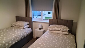 Une chambre double avec deux lits, chacun agrémenté de draps à motifs de cœur, une table de chevet avec une lampe et une fenêtre avec des rideaux.