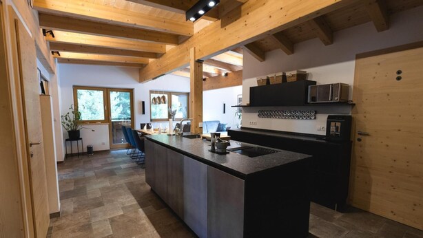 A modern kitchen with a large island, wooden beams, and a view of the outdoors. - Penthouse at 1900 Meters Above sea Level (Soelden)